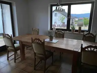 Heller Essbereich mit großem Holztisch, rustikalen Stühlen und Fensterblick auf die umliegende Hügellandschaft.