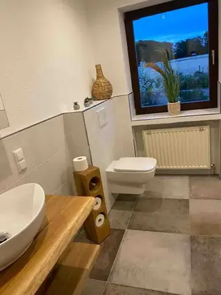 Zeitgemäß gestaltetes Badezimmer mit Aufsatzwaschbecken auf Echtholz, wandhängendem WC und Fensterblick.