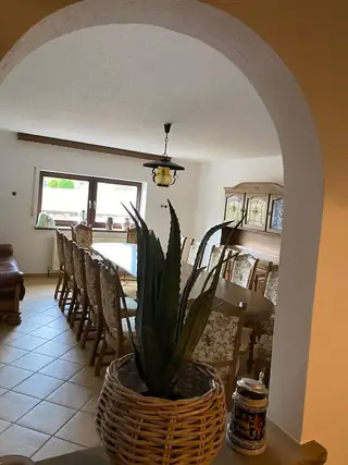 Großzügiges Esszimmer mit langem Holztisch, vielen Stühlen und traditionellem Buffetschrank, gesehen durch einen Rundbogen.