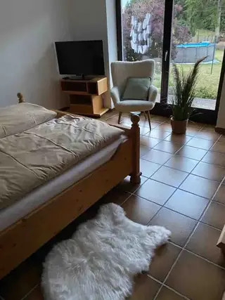 Gemütliches Schlafzimmer mit Holzbett, Fernseher und Glastür mit Blick auf Garten und Pool.