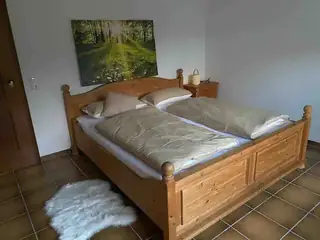 Einladendes Schlafzimmer mit Massivholz-Doppelbett, Waldbild, Nachttischlampe und weißem Fellvorleger.